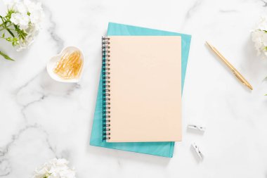 Boş kağıt defter, beyaz çiçekler ve mermer arka plan üzerinde kadınsı aksesuarlar ile modern ev ofis masası çalışma alanı. Düz yatıyordu, üstten bak, tepede. Kadın çalışma alanı kavramı.