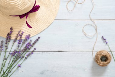 Hasır şapka yuvarlak çerçeve, lavanta çiçekleri, rustik mavi ahşap arka plan üzerinde ip. Düz döşeme, üst görünüm, kopyalama alanı. Yaz moda konsepti.