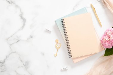Boş kağıt defter, pembe ortanca çiçek, pastel battaniye ve mermer arka plan üzerinde altın aksesuarlar ile modern ev ofis masası işyeri. Güzellik blogger çalışma alanı kavramı. Flatlay, üst görünüm.