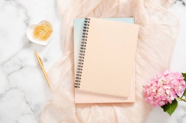 Boş kağıt defter, pembe ortanca çiçek, pastel battaniye ve mermer arka plan üzerinde şık aksesuarlar ile üst görünüm ev ofis masası masa. Kadınsı arka plan, moda blogger çalışma alanı kavramı
