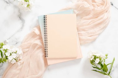 Boş kağıt defter, beyaz çiçekler, mermer arka plan üzerine pastel battaniye. Düz yatıyordu, üst görünüm ev ofis masası. Güzellik blogger çalışma alanı kavramı.