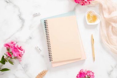 Boş kağıt defter, pembe çiçekler, pastel battaniye ve mermer arka plan üzerinde altın aksesuarlar. Düz yatıyordu, üst görünümü gül altın ev ofis masası. Güzellik blogger çalışma alanı kavramı.