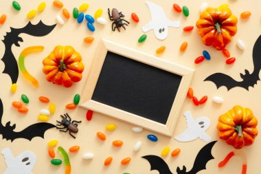 Halloween süslemeleri, pastel bej arka plan üzerinde siyah kağıt kart mockup ile resim çerçevesi. Dekoratif balkabağı, kağıt yarasalar, örümcekler, şekerler. Cadılar Bayramı konsepti. Düz döşeme, üst görünüm, kopyalama alanı