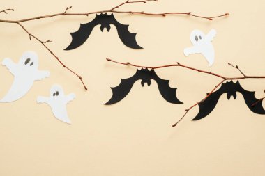 Pastel bej arka plan üzerinde Halloween kağıt süslemeleri. Siyah yarasalar ve beyaz hayaletler dalda oturuyorlar. Cadılar Bayramı konsepti. Düz döşeme, üst görünüm, kopyalama alanı