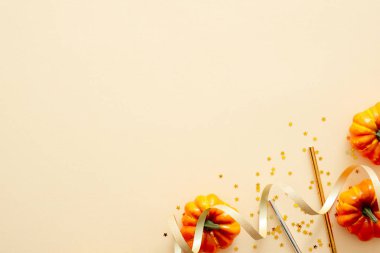 Cadılar Bayramı kompozisyonu. Cadılar Bayramı süslemeleri, kabaklar, konfeti, pastel bej arka plan üzerinde altın kurdele. Cadılar Bayramı parti davetiye kartı mockup. Düz döşeme, üst görünüm, kopyalama alanı