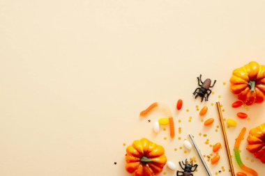 Cadılar Bayramı kompozisyonu. Cadılar Bayramı süslemeleri, kabaklar, şekerler, pastel bej arka plan örümcekler. Cadılar Bayramı konsepti. Düz döşeme, üst görünüm, kopyalama alanı