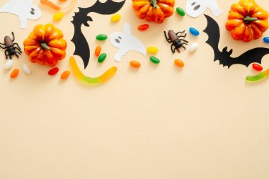 Cadılar Bayramı kompozisyonu. Cadılar Bayramı süslemeleri, yarasalar, kabaklar, şekerler, pastel bej arka plan örümcekler. Cadılar Bayramı konsepti. Düz döşeme, üst görünüm, kopyalama alanı