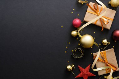 Modern kırmızı ve altın Noel süslemeleri, süs eşyaları, koyu siyah arka plan üzerinde hediye kutuları. Düz döşeme tasarımı, üst görünüm, kopyalama alanı. Zarif Noel tebrik kartı mockup.