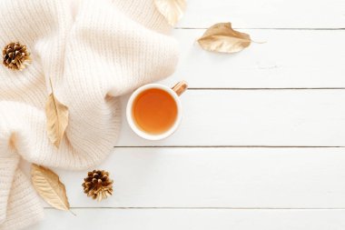 Örgü ekose, çay bardağı, sonbahar yaprakları, ahşap beyaz arka plan üzerinde koniler ile rahat ev masası masa. Üst görünüm, düz döşeme, kopyalama alanı. Sonbahar kompozisyonu. İskandinav hygge tarzı kavramı.