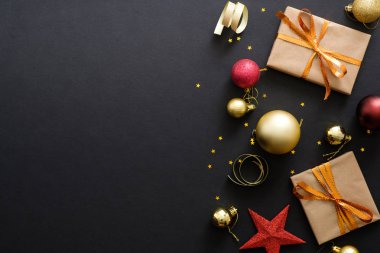Modern kırmızı ve altın Noel süslemeleri, süs eşyaları, hediye kutuları, koyu siyah arka plan konfeti yıldız. Düz döşeme tasarımı, üst görünüm, kopyalama alanı. Zarif Noel tebrik kartı mockup.