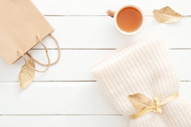 Örgü ekose ile rahat ev masası masa, çay bardağı, sonbahar yaprakları, ahşap beyaz arka plan üzerinde kraft kağıt torba. Üst görünüm, düz döşeme, kopyalama alanı. Sonbahar kompozisyonu. İskandinav hygge tarzı. Sonbahar satış konsepti.