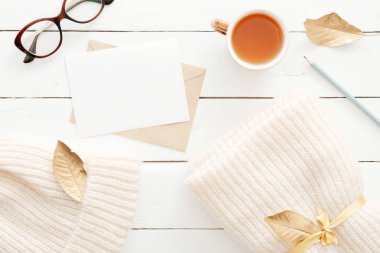 Örgü ekose ile rahat ev masası masa, çay bardağı, sonbahar yaprakları, ahşap beyaz arka plan üzerinde boş kart ile mektup. Üst görünüm, düz döşeme, kopyalama alanı. Sonbahar kompozisyonu. İskandinav hygge tarzı kavramı.