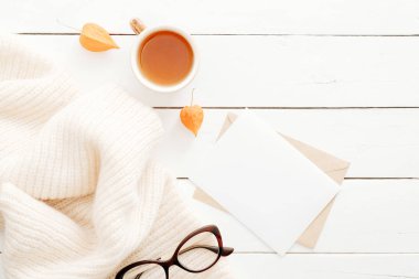 Sonbahar kompozisyonu. Boş mektup, çay bardağı, gözlük, ahşap beyaz arka plan üzerine örme ekose ile kadınsı çalışma alanı. Üst görünüm, düz döşeme, kopyalama alanı. İskandinav hygge tarzı kavramı.