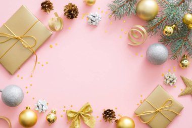 Altın ve gümüş topları, köknar ağacı dalları, süslemeleri, hediye kutuları, pastel pembe arka plan üzerinde çam kozalağı yapılmış Noel çerçevesi. Düz döşeme, üst görünüm, kopyalama alanı. Noel, kış, Yeni Yıl konsepti