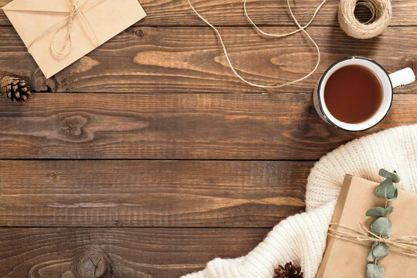 Sonbahar flatlay kompozisyon. Çerçeve zanaat kağıt zarf, çay fincan, ip, hediye kutusu, ahşap arka plan üzerinde beyaz örme eşarp yapılmış. Sonbahar hygge tarzı masa veya kış tatili konsepti.