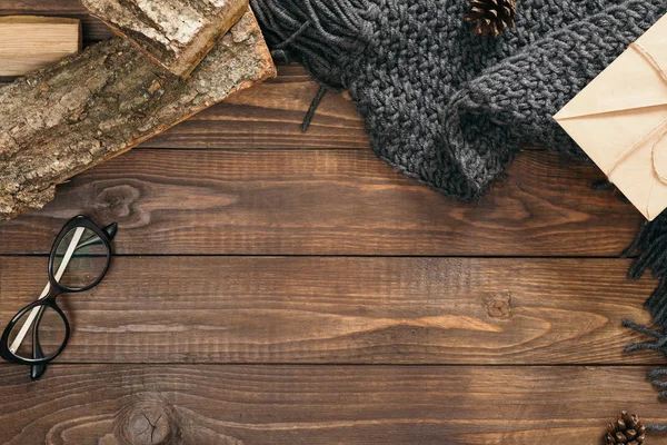 Composición plana con bufanda de punto gris, leña, sobre de papel artesanal, vasos sobre fondo de madera. Acostado plano, vista superior, arriba. Acogedora mesa de escritorio de otoño —  Fotos de Stock