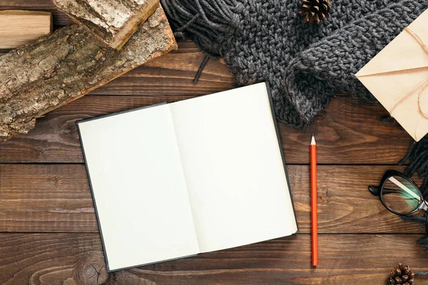 Nordic hygge tarzı flatlay kompozisyon, Kitap boş sayfaları, moda kadınsı örme eşarp, hediye kutusu, ahşap arka plan üzerinde yakacak odun ile. Düz yatıyordu, üstten bak, tepede. Rahat ev ofis masası