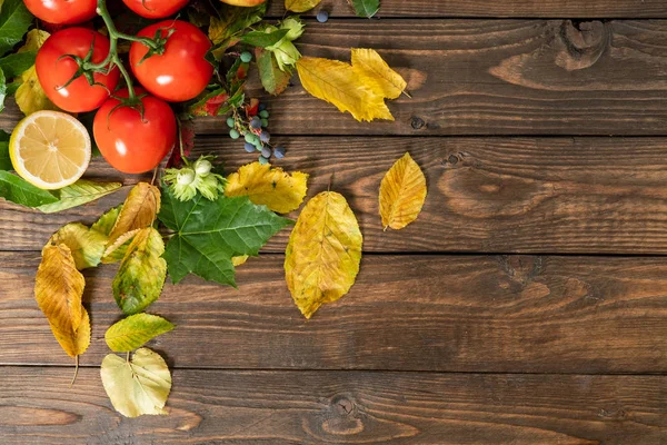 Flatlay sonbahar kompozisyon. Domates, limon, sonbahar düşmüş yapraklar tahta masanın üzerine. Düz döşeme, üst görünüm, kopyalama alanı. Tarım çeşitleri, sonbahar hasat konsepti
