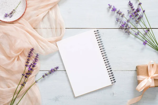 Boş kağıt not defteri, pastel pembe renkli battaniye, lavanta çiçekleri ve rustik mavi ahşap arka plan üzerinde hediye kutusu. Üst görünüm, ihale minimal düz döşeme tarzı kompozisyon. Moda blogger çalışma alanı masası.