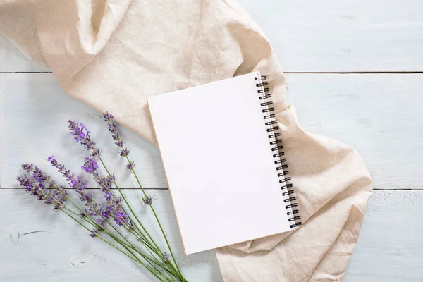 Boş kağıt not defteri, lavanta çiçeği, rustik mavi ahşap arka plan üzerine pastel bej battaniye ile Flatlay kompozisyon. Düz yatıyordu, üst görünüm natürmort kavramı.