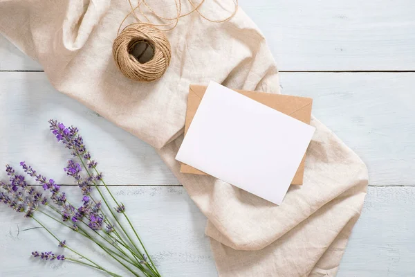 Flatlay flores de lavanda, manta beige pastel, sobre artesanal, maqueta de tarjetas de papel en blanco, cordel sobre fondo rústico de madera azul. Escritorio femenino. Acostado plano, vista superior, arriba. Concepto de moda de verano — Foto de Stock