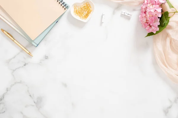 Elegante composición con flor de hortensia rosa, manta pastel, bloc de notas de papel y accesorios sobre fondo de mármol. Plano, vista superior, techo —  Fotos de Stock