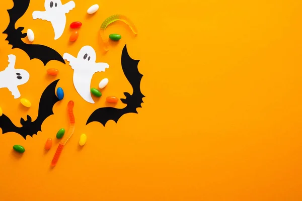 Happy halloween holiday concept. Halloween decorations, bats, ghosts, candy on orange background. Halloween party greeting card mockup with copy space. Flat lay, top view, overhead.