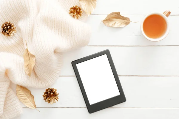 Sonbahar kompozisyonu. Örme eşarp, çay bardağı, koniler, boş ekranlı tablet ebook ile kadınsı masa masa, ahşap arka plan üzerinde sonbahar yaprakları. Düz yatıyordu, üstten bak. İskandinav, hygge, rahat ev konsepti