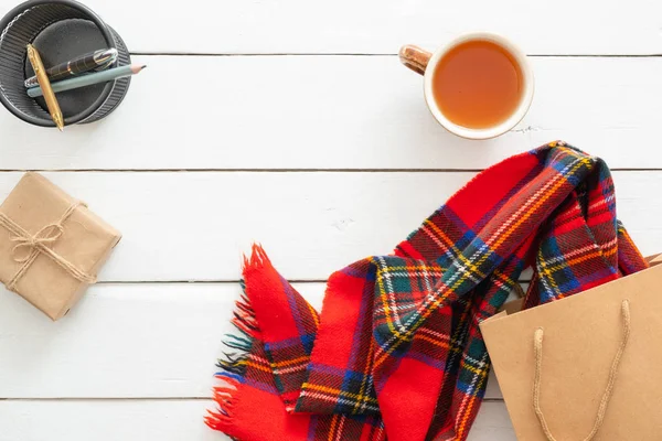 Sonbahar kompozisyonu. Kırmızı eşarp, çay bardağı, hediye kutusu, ahşap beyaz arka plan üzerinde alışveriş çantası ile kadınsı masa masa. Düz yatıyordu, üstten bak. İskandinav, hygge, rahat ev konsepti