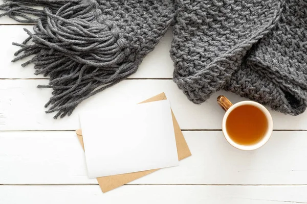 Ahşap beyaz arka plan üzerinde örgü ekose, çay bardağı, mektup, boş kağıt kart ile üst görünüm rahat ev masası. Düz yatıyordu, üstten bak. İskandinav, hygge, konfor konsepti
