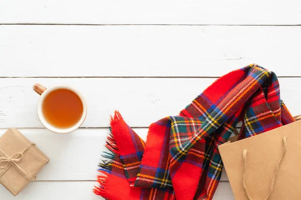 Sonbahar kompozisyonu. Kırmızı eşarp, çay bardağı, hediye kutusu, ahşap beyaz arka plan üzerinde alışveriş çantası ile kadınsı masa masa. Düz yatıyordu, üstten bak. İskandinav, hygge, rahat ev konsepti