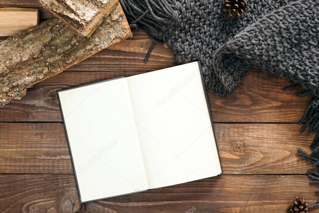 Scandinavian hygge style flatlay composition, Book with empty pages, fashion feminine knitted scarf, firewood on wooden background. Flat lay, top view, overhead. Cozy home office desk table
