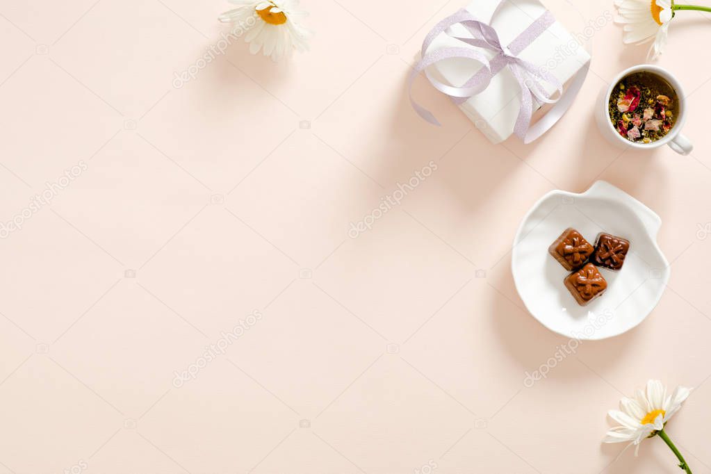 Romantic flatlay composition with gift box, herbal tea, ribbon, daisy chamomile flower on pastel pink background. Feminine home office desk concept. Flat lay, top view