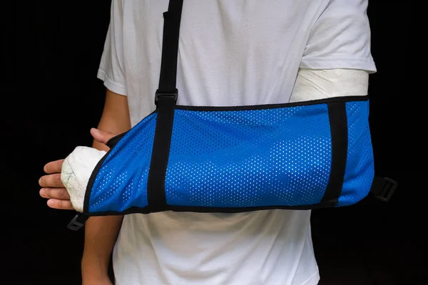 Man with broken arm wrapped medical cast plaster and blue bandage. Fiberglass cast covering the wrist, arm, elbow after sport accident, isolated on black