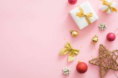 Kopya alanı ile pastel pembe arka plan üzerinde Flatlay Noel tatili kompozisyon. Üst görünüm Xmas süslemeleri, kırmızı ve altın topları, hediye kutusu, yıldız, yay. Noel tebrik kartı mockup, afiş şablonu