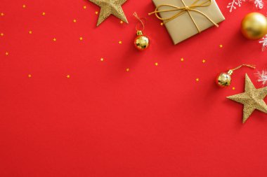 Kırmızı arka plan üzerinde altın Noel süslemeleri üst görünümü. Düz hediye kutusu, yıldız, topları, ışıltılı konfeti yatıyordu. Yeni Yıl tebrik kartı mockup, kopya alanı. Noel kartpostal şablonu tasarımı.