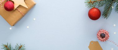 Mavi arka plan üzerinde Noel flatlay kompozisyon. Üst görünüm hediye kutusu, kırmızı toplar, köknar ağacı dalı, ip, kraft kağıt etiketi, glitter konfeti yıldız. Xmas veya Metin için kopya alanı ile Yeni Yıl afiş mockup.