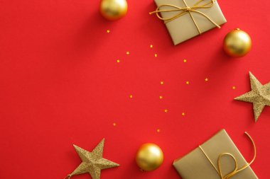 Kopya alanı ile kırmızı arka plan üzerinde Noel altın süslemeleri. Düz altın hediye kutusu, süs eşyaları, yıldızlar, ışıltılı konfeti yatıyordu. Noel posteri mockup, tebrik kartı şablonu, web sitesi başlık kahraman
