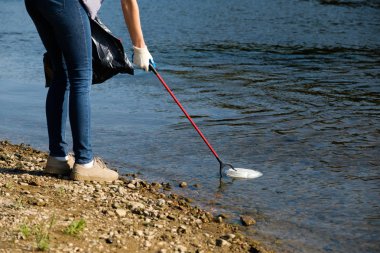 Gönüllü kadın nehrin kıyısında plastik çöp topluyor. Temizlik ortamı kavramı