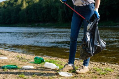 Sahilde plastik çöp toplayan gönüllü bir kadın. Temizlik ortamı kavramı