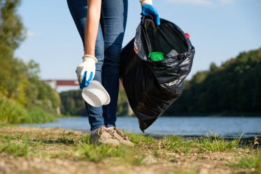 Nehrin kıyısında plastik çöp toplayan gönüllü bir kadın. Temizlik ortamı kavramı