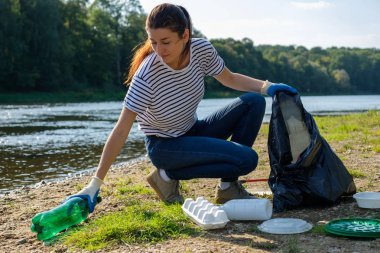 Nehrin kıyısında plastik çöp toplayan gönüllü bir kadın. Temizlik ortamı kavramı