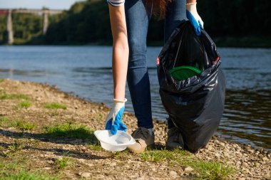 Nehrin kıyısında plastik çöp toplayan gönüllü bir kadın. Temizlik ortamı kavramı