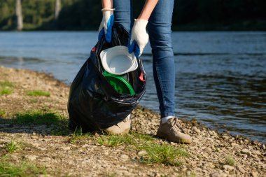 Nehrin kıyısında plastik çöp toplayan gönüllü bir kadın. Temizlik ortamı kavramı