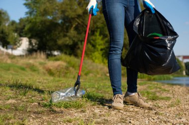 Gönüllü kadın nehrin kıyısında plastik çöp topluyor. Temizlik ortamı kavramı