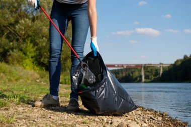 Gönüllü kadın nehrin kıyısında plastik çöp topluyor. Temizlik ortamı kavramı