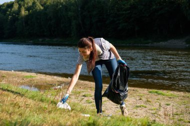 Nehrin kıyısında plastik çöp toplayan gönüllü bir kadın. Temizlik ortamı kavramı
