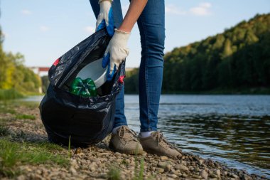 Nehrin kıyısında plastik çöp toplayan gönüllü bir kadın. Temizlik ortamı kavramı