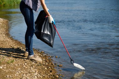 Gönüllü kadın nehrin kıyısında plastik çöp topluyor. Temizlik ortamı kavramı