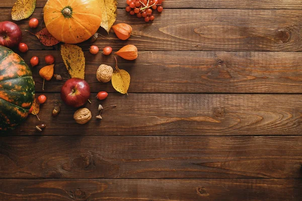 Harvest or Thanksgiving background with pumpkins, dried fall leaves, apples, red berries, walnuts on wooden table. Flat lay composition, top view, copy space